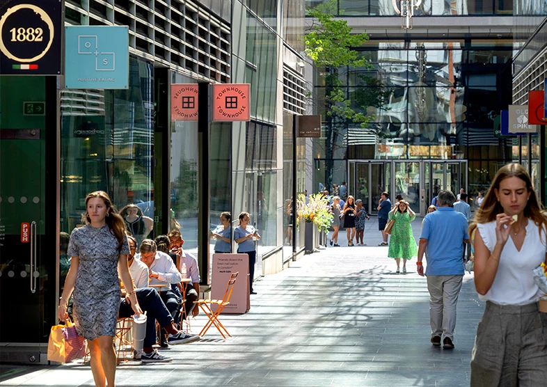 New Street Square located in Midtown London
is a modern urban shopping and dining street
with glass-fronted buildings, outdoor seating,
and people walking or sitting at tables. The area
is bright and lively, with colourful signs hanging
above storefronts. The atmosphere is relaxed
and contemporary.