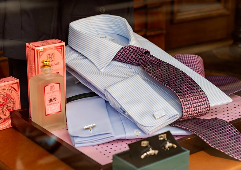 A man's smart, light blue collared shirt with a
pink polka dot tie is folded up in the window of
Geo. F. Trumper. Alongside the shirt are a
range of Geo. F. Trumper luxury men's shaving
products including soap and cologne.
