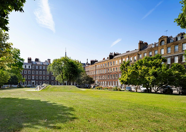 View of Lincoln’s Inn Fields in London with
historic Georgian buildings, green lawns known
as New Square and trees under a clear blue
sky.
