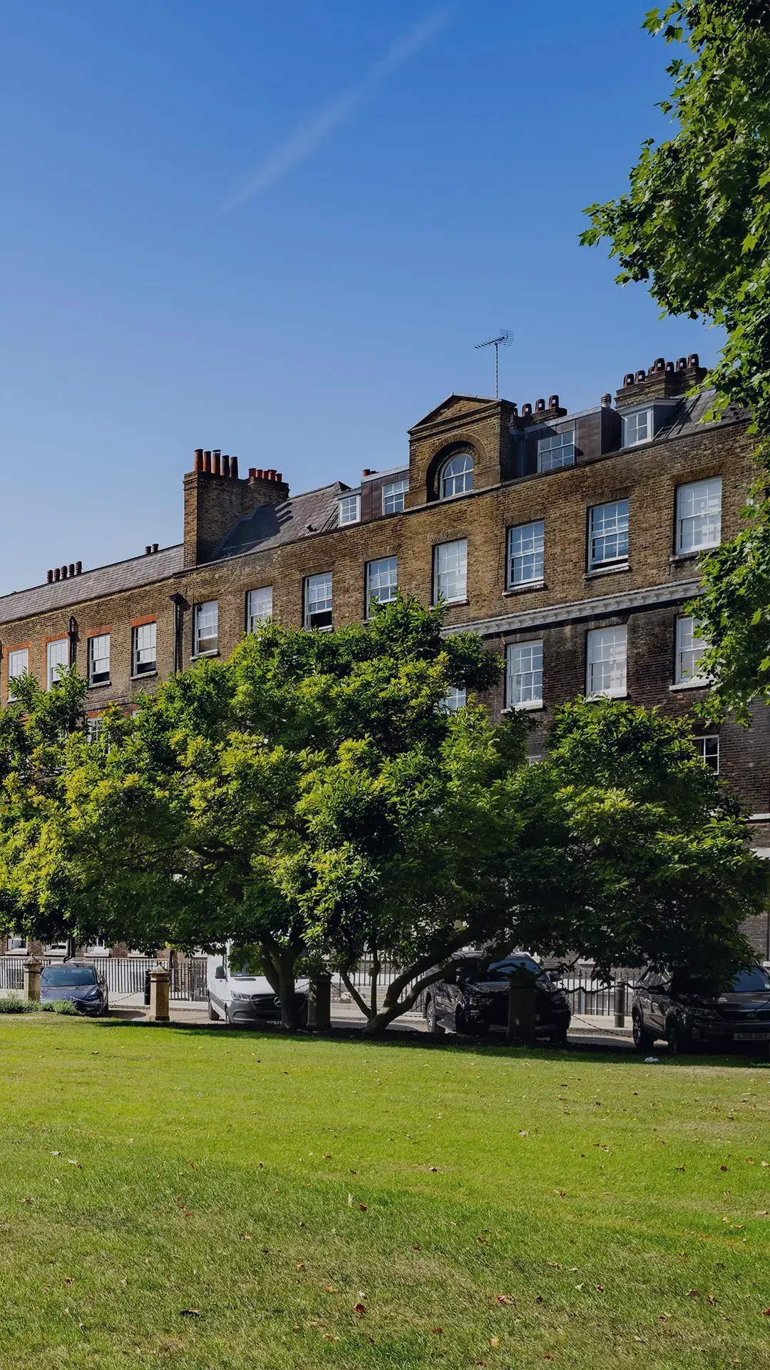 View of Lincoln’s Inn Fields in London with
historic Georgian buildings, green lawns known
as New Square and trees under a clear blue
sky.
